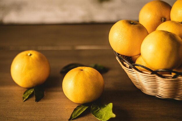 Closeup of fresh oranges inside a woven basket and on top of the wooden table