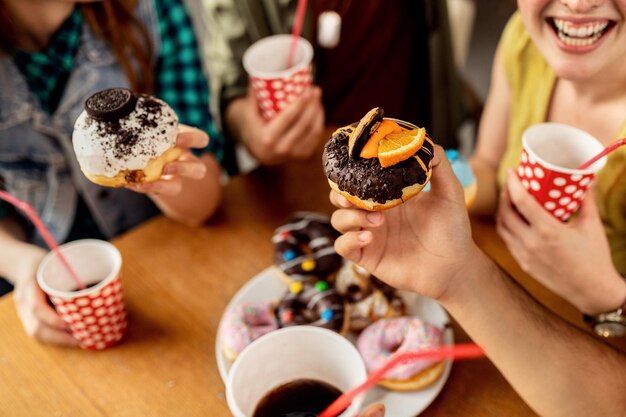 Крупный план друзей, наслаждающихся вкусными глазированными пончиками на десерт