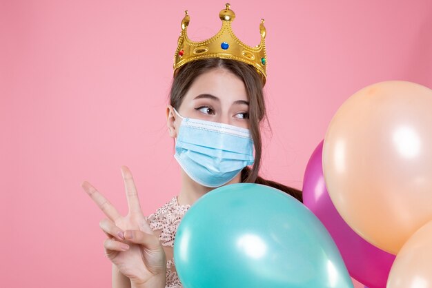 Closeup front view cute party girl with crown holding balloons making victory sign