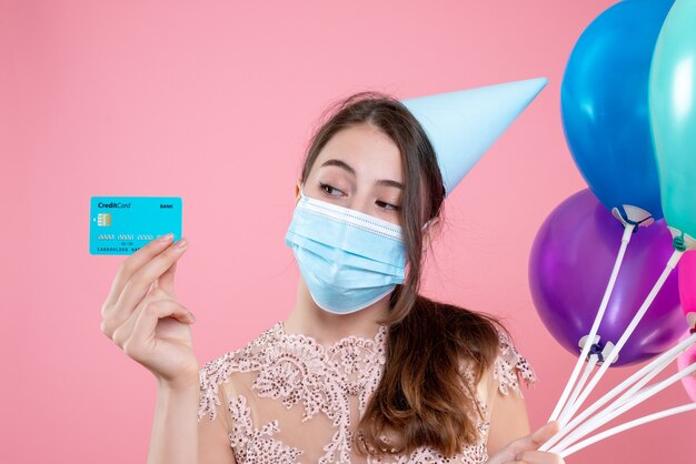 Closeup front view cute party girl with crown and mask holding balloons and card