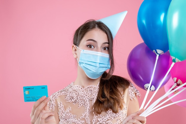 Closeup front view cute party girl with medical mask holding balloons and card