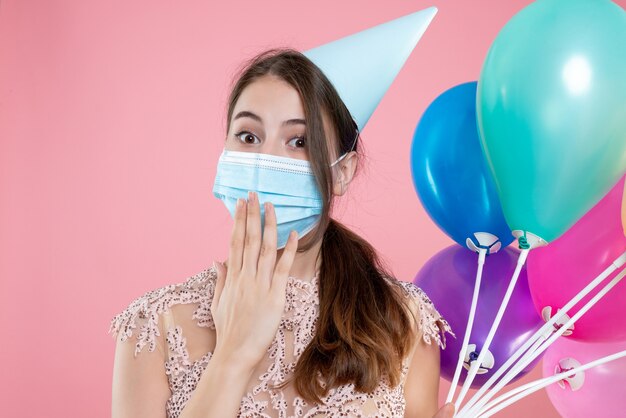 Closeup front view party girl with crown and mask holding balloons