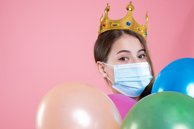 Closeup front view party girl with crown and medical mask holding balloons