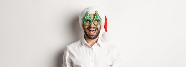 クリスマス パーティーのメガネとサンタの帽子を身に着けている驚いた顔で左を見て変な男のクローズ アップ