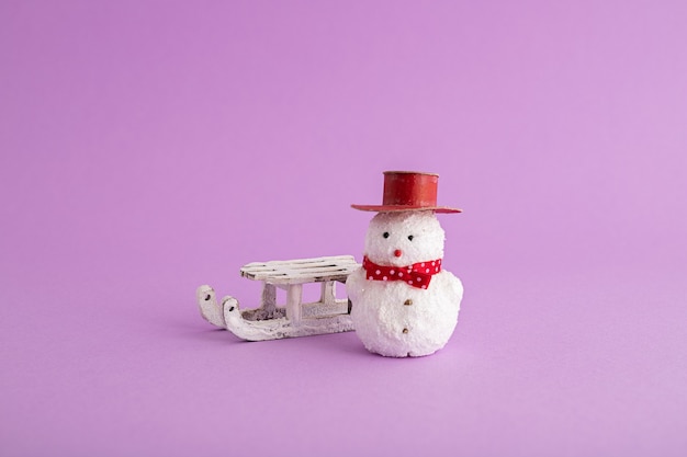 Closeup of a funny snowman and a Christmas sleigh in the purple background