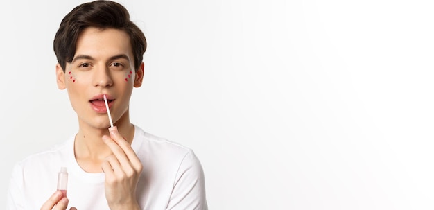 Closeup of gender fluid person with glitter on face applying lip gloss lipstick and looking at camer