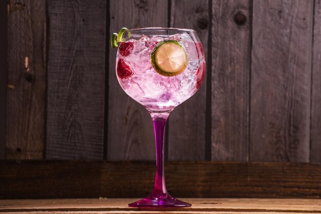 Closeup of gin and tonic with ice and raspberries against a wooden background