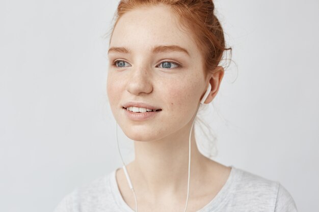 Closeup of ginger woman listening to streaming music with wired earphones.