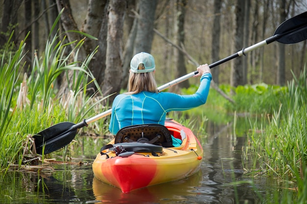 Free photo closeup of a girl kayaking on a small river surrounded by greenery under the sunlight at daytime