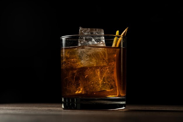 Closeup of a glass of old fashioned cocktail with ice on a wooden table with a blurry background