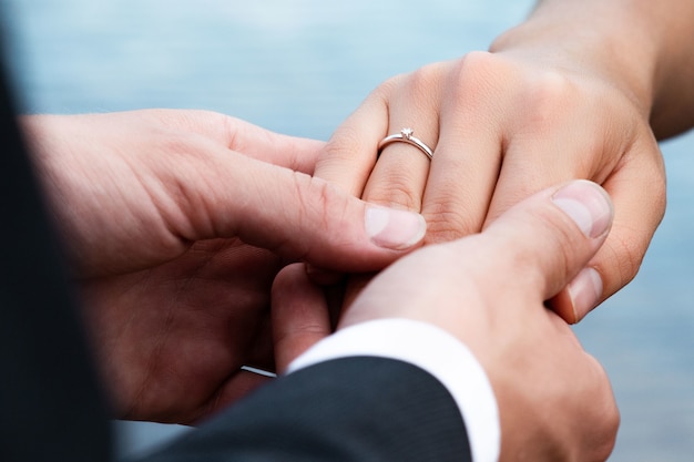 Closeup of a groom putting a ring on the finger of the bride under the lights