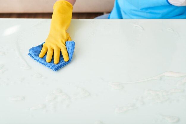 Closeup of hand in glove cleaning table with foam detergent