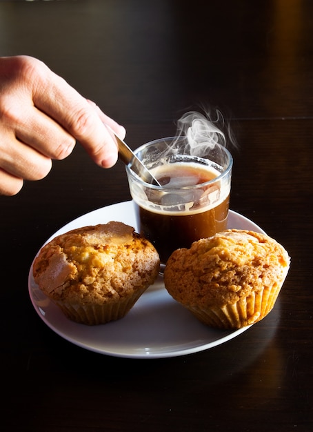 Closeup of hand mixing coffee with a spoon next to fresh muffins