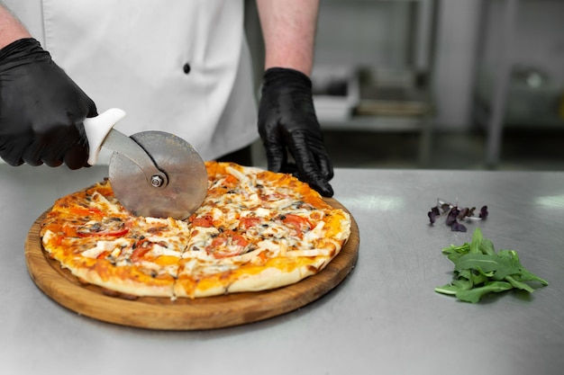 シェフのクローズアップの手は、キッチンで作りたてのピザのスライスをカットします