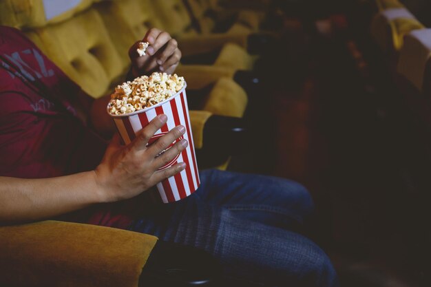 Крупным планом рука собирает попкорн из ведра для попкорна, которое несет во время просмотра фильма в кинотеатре.