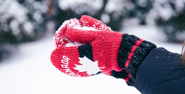 赤いカナダのミトンの手のクローズアップは雪から雪玉を作ります