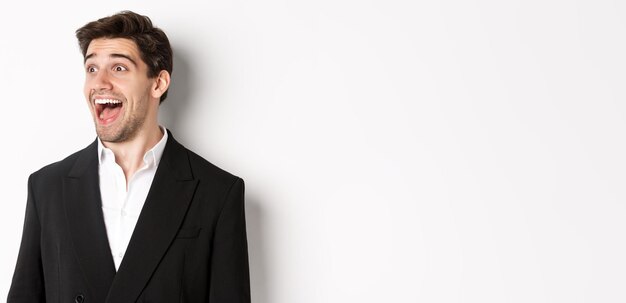 Closeup of handsome male entrepreneur in suit looking left and smiling amazed standing against white