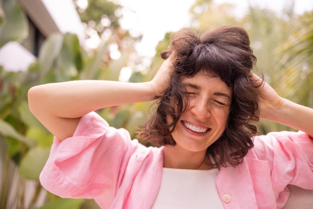 Closeup of happy european young woman smiling with eyes closed messing up dark hair outdoors Concept of emotions lifestyle