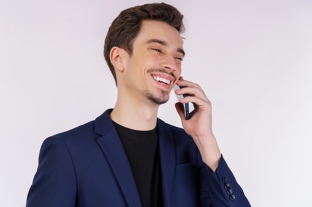 Primo piano di felice uomo d'affari bello parlando dal telefono cellulare e in piedi isolato su sfondo bianco