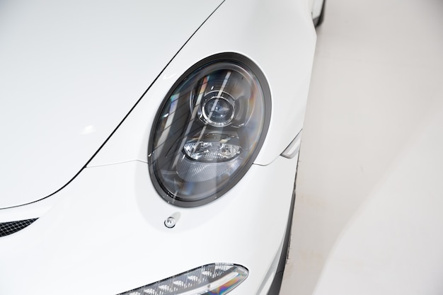 Closeup of the headlight of a white luxury car under the lights against a grey background