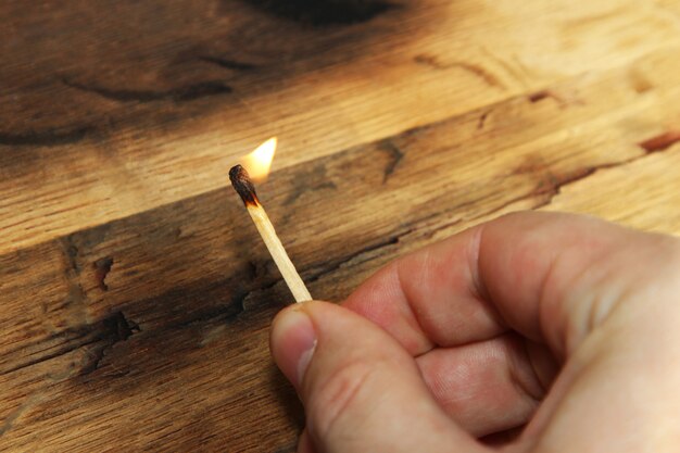 Closeup high angle shot of a person holding a burning matchstick over a wooden surface