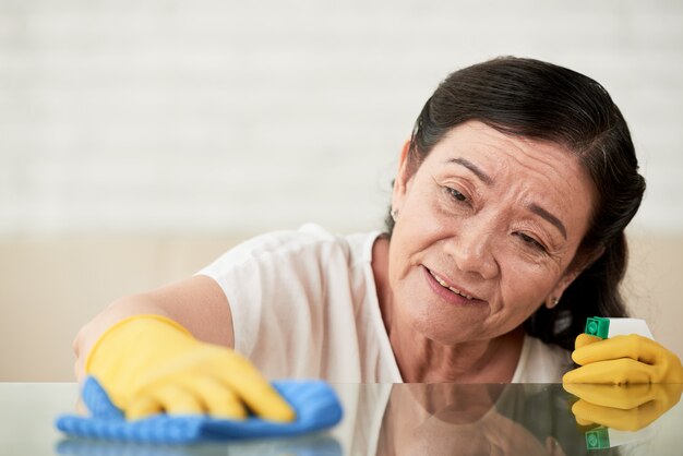 Closeup of housemaid polishing glass table with glass spray cleaner