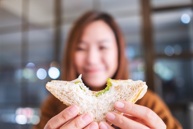 Closeup image of a beautiful woman holding and biting a piece of whole wheat sandwich