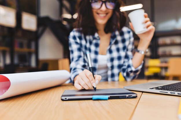 Closeup image hand of young brunette woman designing on table in library surround work stuff. Laptop, creative work, graphic design, freelancer, smart student.