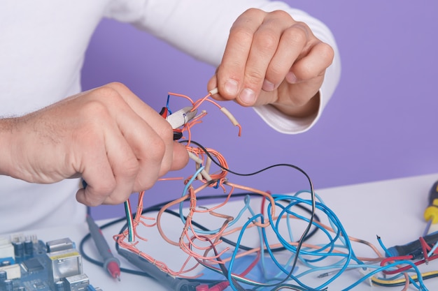 Closeup indoor picture of man hands holding side cutting pillers and conductors, doing his work in proper way, making repair by himself