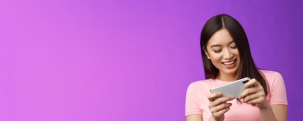 Бесплатное фото Крупным планом радостная привлекательная азиатская женщина-брюнетка весело проводит время, играя в смартфон, смеясь