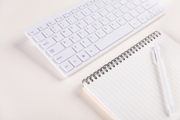 Крупным планом клавиатуры и блокнота с ручкой на белом столе - концепция работы
