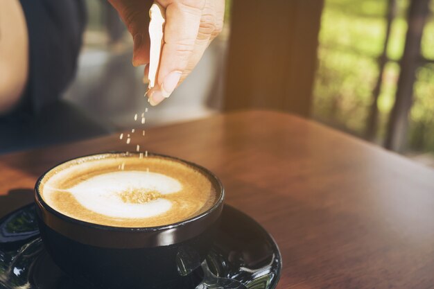 Closeup of lady pouring sugar while preparing hot coffee cup