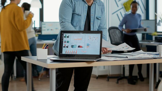 Closeup of laptop screen with enterprise resource planning showing moving charts and growing turnover in busy startup office. Selective focus on portable computer with business mangement software.