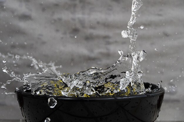 Closeup of a lemon and splashing water in a black bowl under the lights against a grey background