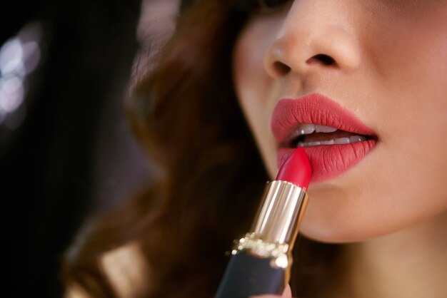 Closeup of lipstick touching plump red female lips 