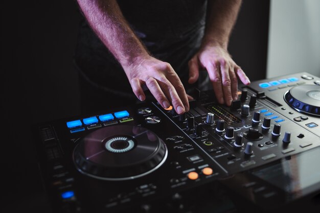 Closeup of a male DJ working under the lights against a dark background in a studio