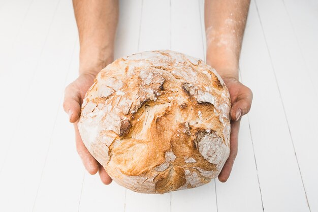 Closeup of male hands put fresh bread on an old rustic table on black background with copy space for your text