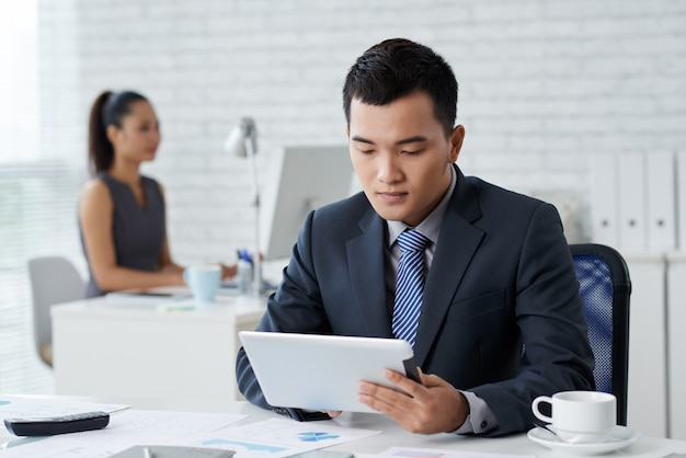 Closeup of man in formalwear sitting at the office desk and working at tablet PC