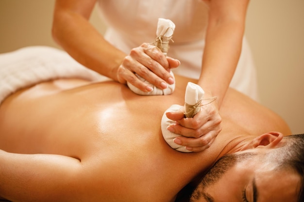 Closeup of man getting back massage with detox herbal balls at health spa