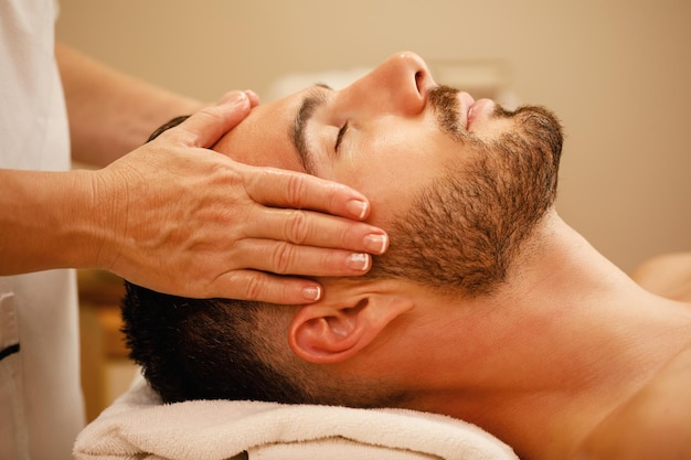 Крупным планом мужчина получает массаж головы и расслабляется с закрытыми глазами в спа-центре