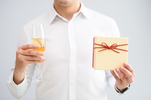 Closeup of man holding glass with champagne and gift box
