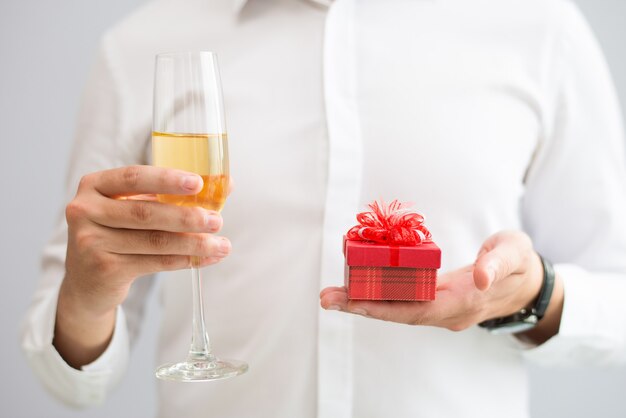 Крупным планом мужчина держит бокал с шампанским и небольшой подарочной коробке
