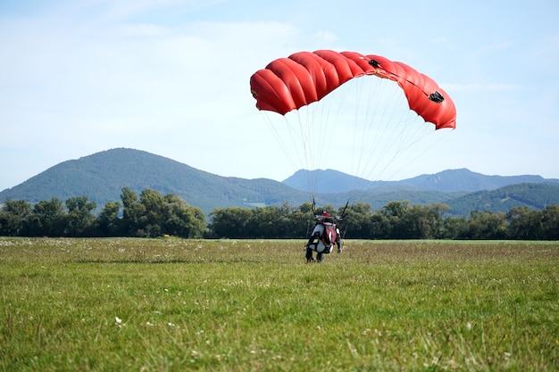 Closeup of a man parachuting near the ground with a red parachute during daylight