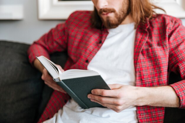 Крупным планом человека в клетчатой рубашке, чтение книги у себя дома
