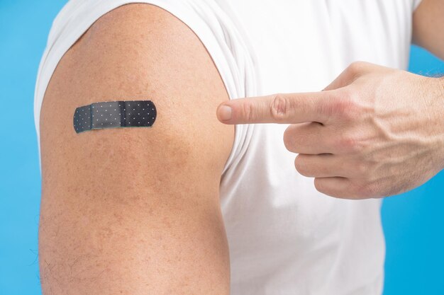 Closeup a man pointing finger on his shoulder with a band aid on it after receiving the Covid19 vaccine Vaccine against COVID19 or coronavirus Aging male skin Fair skin men Healthcare concept