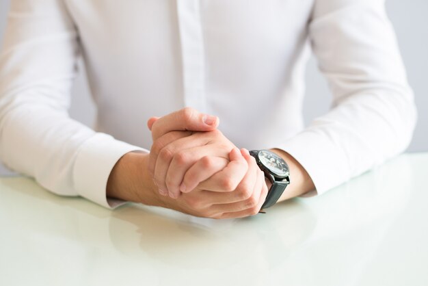 Closeup of man sitting at desk with his hands clasped