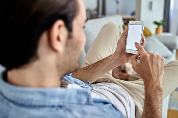 ソファでリラックスしながら携帯電話でネットサーフィンをしている男性のクローズアップフォーカスは空白のデバイス画面にありますコピースペース