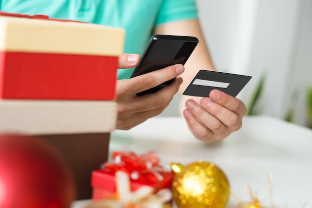 クレジットカード、スマートフォン、クリスマスプレゼントを持つ男のクローズアップ