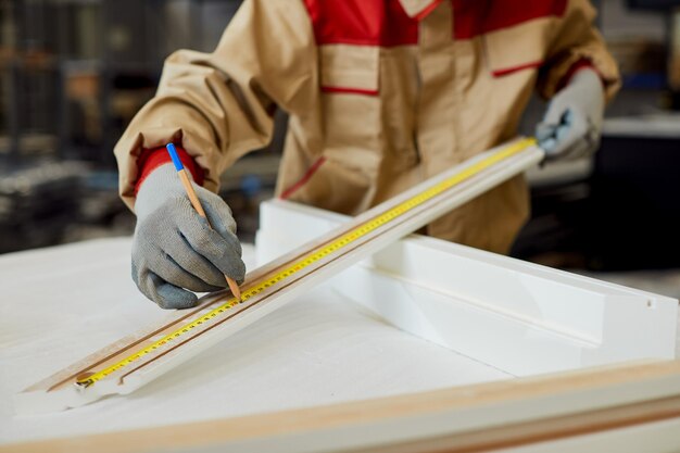 Closeup of manual worker marking measurements on a piece of wood at carpentry workshop
