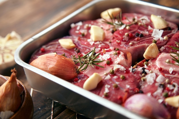 周りの鋼鍋スパイスの肉のクローズアップ：ニンニク、ローズマリー、玉ねぎ